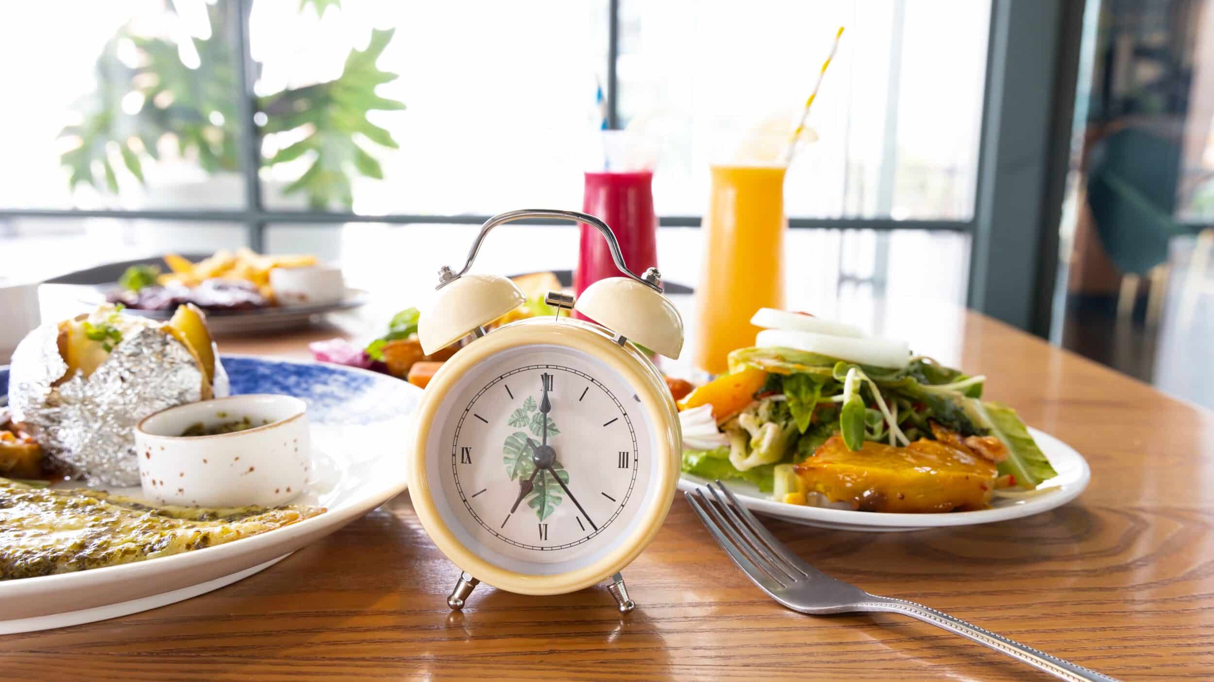 Horloge au centre de la table avec une asiette des légumes et 2 smoothies, ainsi q'une asiette vide à côté